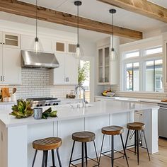 a large kitchen with white cabinets and wooden stools in front of an island counter