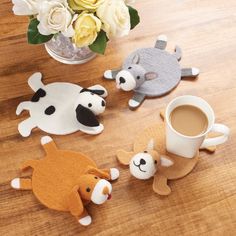 four felt animals sitting on top of a wooden table next to a cup of coffee