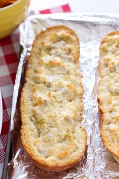 two pieces of bread sitting on top of tin foil next to a bowl and knife