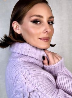 a woman in a purple sweater posing for a photo with her hand on her shoulder