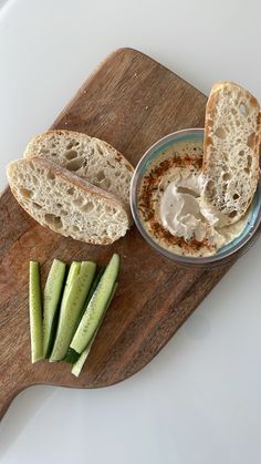 a wooden cutting board topped with sliced cucumbers and bread next to a bowl of dip