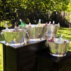 several metal buckets with bottles in them sitting on top of a black table outside