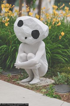 a statue of a person sitting on the ground in front of some plants and flowers