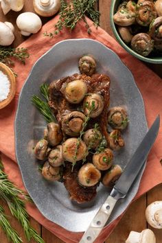 a plate full of cooked mushrooms on a table with garlic and seasoning next to it