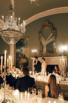 a bride and groom are standing in front of their guests at a dinner table with candles on the tables