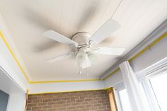 a white ceiling fan mounted on the side of a brick wall next to a window