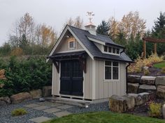 a small shed with a black door and windows on the roof is surrounded by rocks