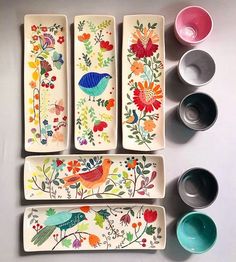 four plates with painted flowers and birds on them next to two empty bowls, one filled with water