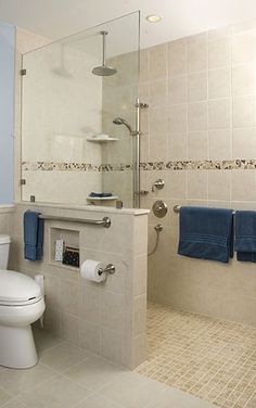 a white toilet sitting next to a walk in shower under a bathroom mirror with blue towels on it