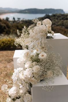 white flowers and greenery are arranged on blocks in the grass near an ocean shore