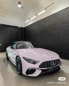 a pink mercedes sports car in a showroom with black walls and white flooring