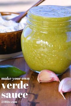 a jar filled with green sauce sitting on top of a wooden table next to garlic