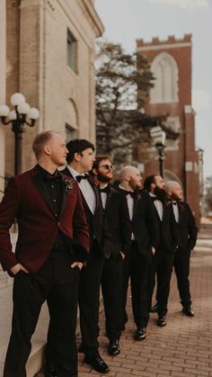 a group of men standing next to each other in front of a brick building wearing black and red tuxedos