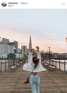 a woman standing on a pier with her arms up in the air and buildings in the background