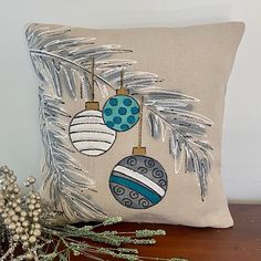 a pillow with ornaments hanging from it on a table next to a plant and christmas tree