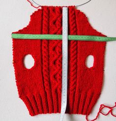 a red knitted sweater with two holes and a measuring tape on the side that shows how to measure it