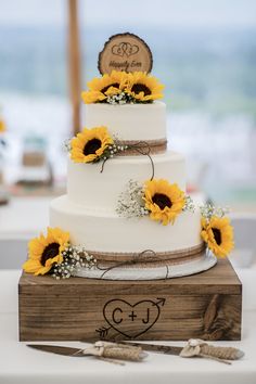 a white wedding cake with sunflowers on top and a wooden sign that says c & u