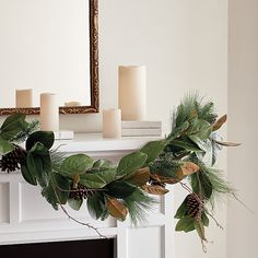 a christmas garland with pine cones, evergreen leaves and candles on a mantel in front of a mirror