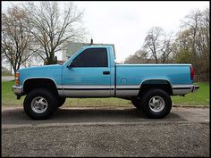 a blue pick up truck parked in a parking lot next to some trees and grass