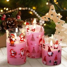 three pink candles with santa's designs on them sitting in front of a christmas tree