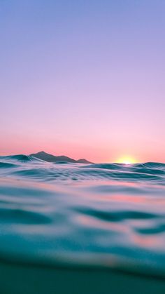 the sun is setting over the ocean as seen from the water's surface, with mountains in the distance