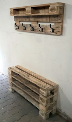 a wooden bench sitting in front of a wall with two hooks on it's side