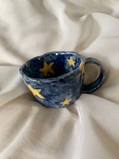 a blue and yellow cup sitting on top of a white cloth covered tablecloth with stars painted on it