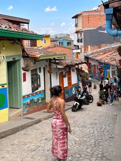 a woman in a pink dress walking down a street next to buildings and parked motorcycles