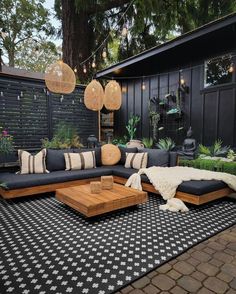 an outdoor living area with black couches, pillows and lights hanging from the ceiling