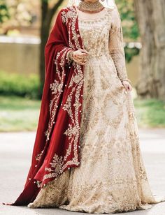 a woman in a white and red bridal gown standing on the street with trees behind her