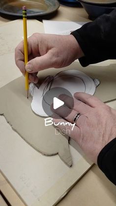 a person is working on a paper plate with a pencil in their left hand and another piece of cardboard behind them