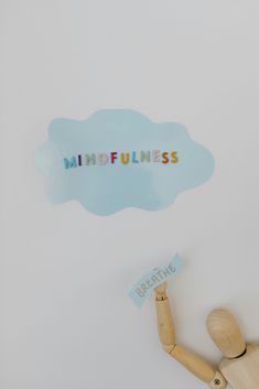 a wooden doll holding a sign that says mindfulness above it is a cloud