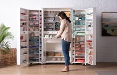 a woman standing in front of a white cabinet filled with lots of drawers and shelves