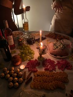 a table topped with lots of food next to candles and wine bottles on top of it