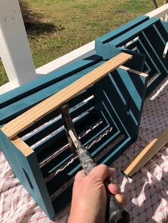 a person using a hammer to cut through the top of a wooden bench with blue shutters