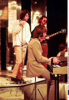 the rolling stones performing on stage in front of microphones and guitar, with two men standing behind them