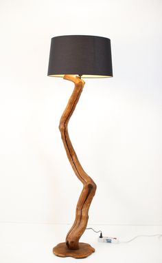 a wooden lamp with a black shade on the base and a white wall behind it