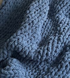 a blue crocheted blanket laying on top of a wooden floor next to a pillow