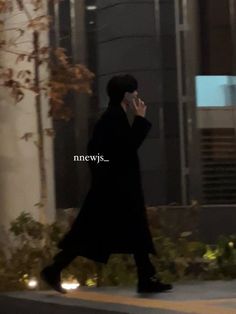 a man walking down the street talking on his cell phone while wearing a long black coat