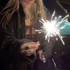 a woman holding a sparkler in her hand and looking at the camera while wearing a black jacket