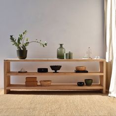 a wooden shelf with vases and bowls on it in front of a white wall