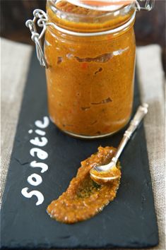 a jar filled with sauce sitting on top of a black board next to a spoon