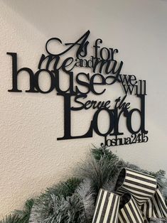 a christmas wreath with black and white striped presents on it, next to a metal sign that reads as for me and my house we will serve the lord