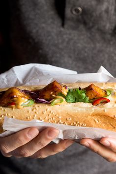 a person holding a long sandwich in their hand with meat and veggies on it