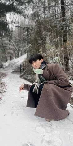 a young man sitting in the snow with his hand on his knee, wearing a coat and scarf