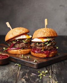 two hamburgers with meat and cheese on a cutting board