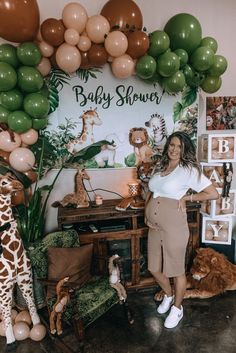 a woman standing in front of a baby shower backdrop with giraffes and balloons