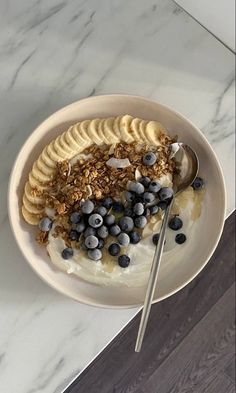 a bowl of yogurt with blueberries and granola on top, next to a spoon