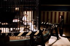 a woman standing in front of a jail cell with bars on the sides and people behind her