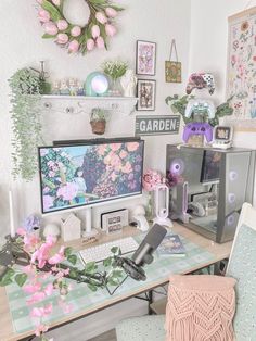 a computer desk topped with two monitors next to a pink flowered wreath on the wall